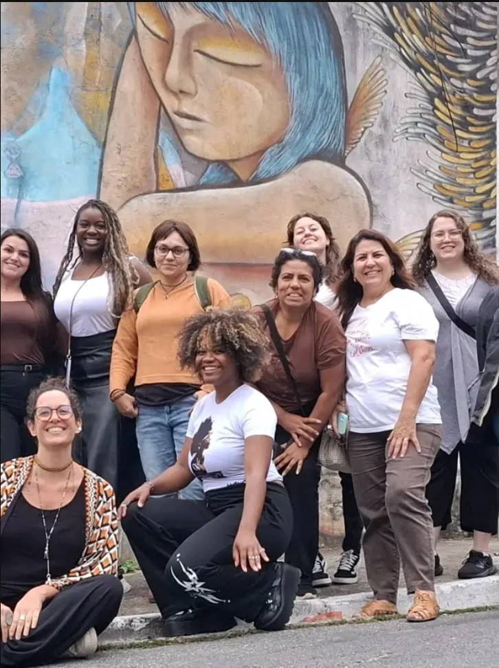 Grupo de mulheres em frente a um mural com figuras femininas na Favela Galeria, Vila Flávia.